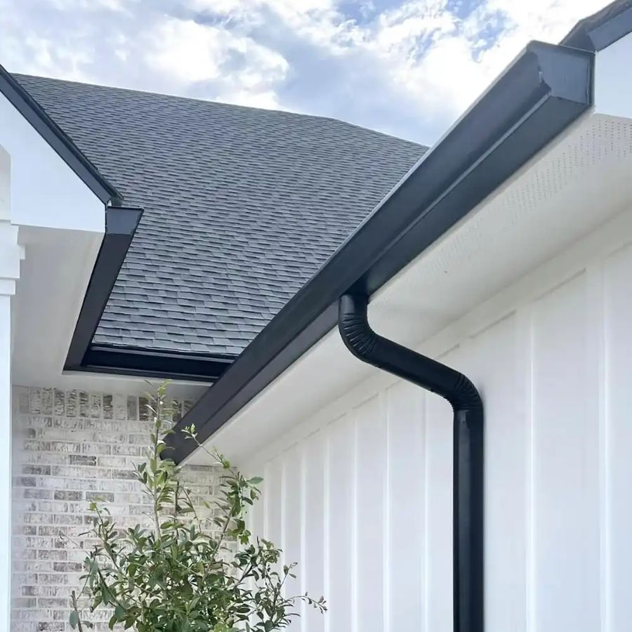 Black gutter and round downspout at the corner of a white board-and-batten wall above painted brick