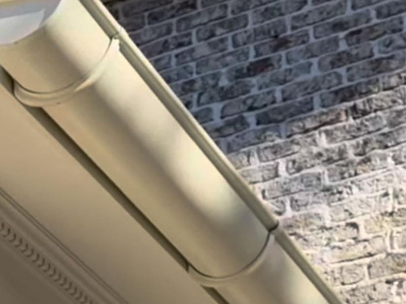 A cream half-round gutter with a beaded edge above molded trim, beside a painted brick wall