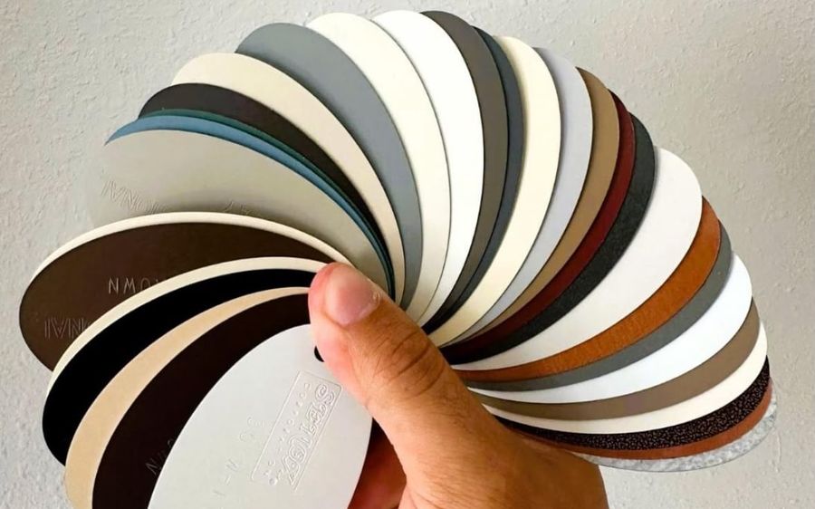 A hand fanning out a ring of gutter color samples, from white and almond through grays, browns and copper tones to black
