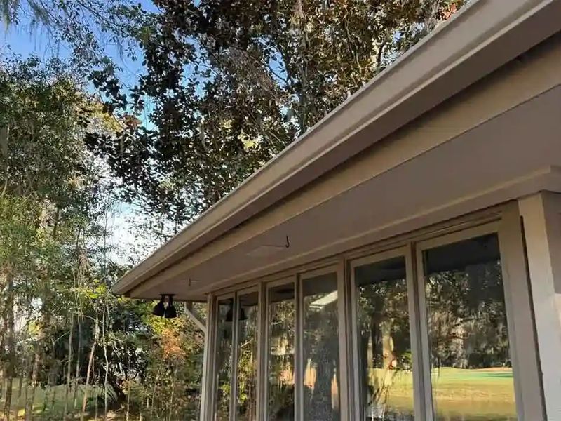 A long almond gutter run along the eave of a glassed-in porch, with trees behind