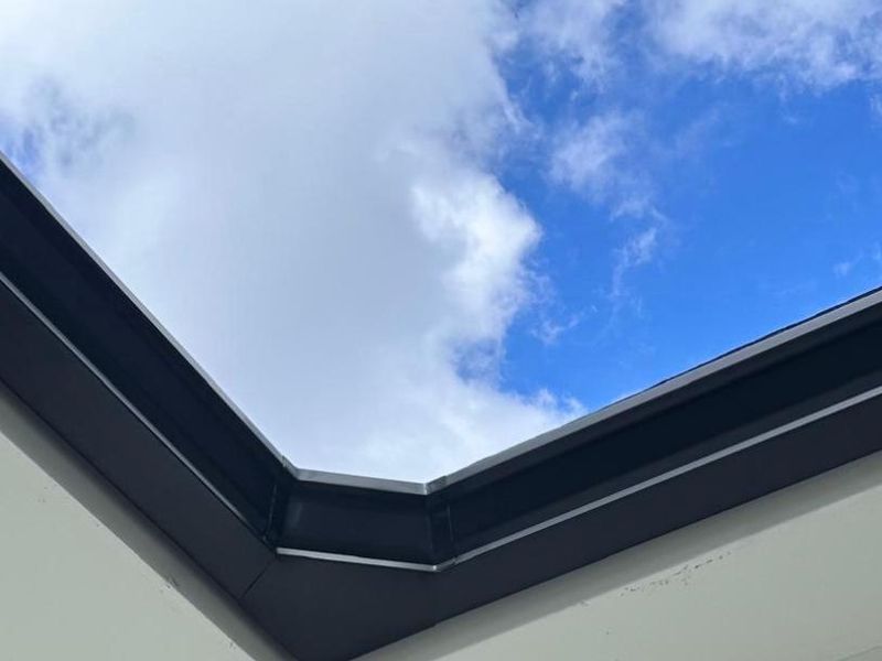 Looking up at a black gutter turning an outside corner above white soffit and siding