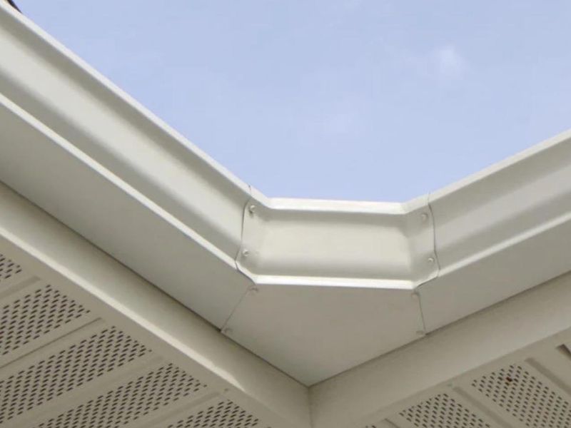 Looking up at a white gutter mitered around a corner above vented white soffit panels