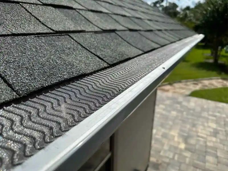 Rhino micro-mesh gutter guard with its wave pattern on a white gutter below dark shingles, with a paver patio below