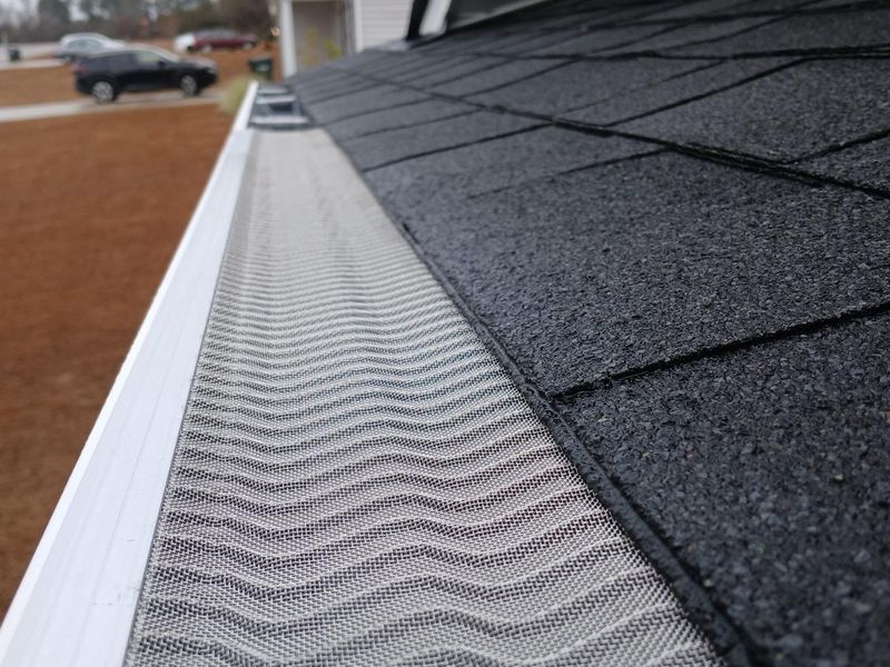 Rhino micro-mesh gutter guard with a wave pattern running along a gutter below dark asphalt shingles