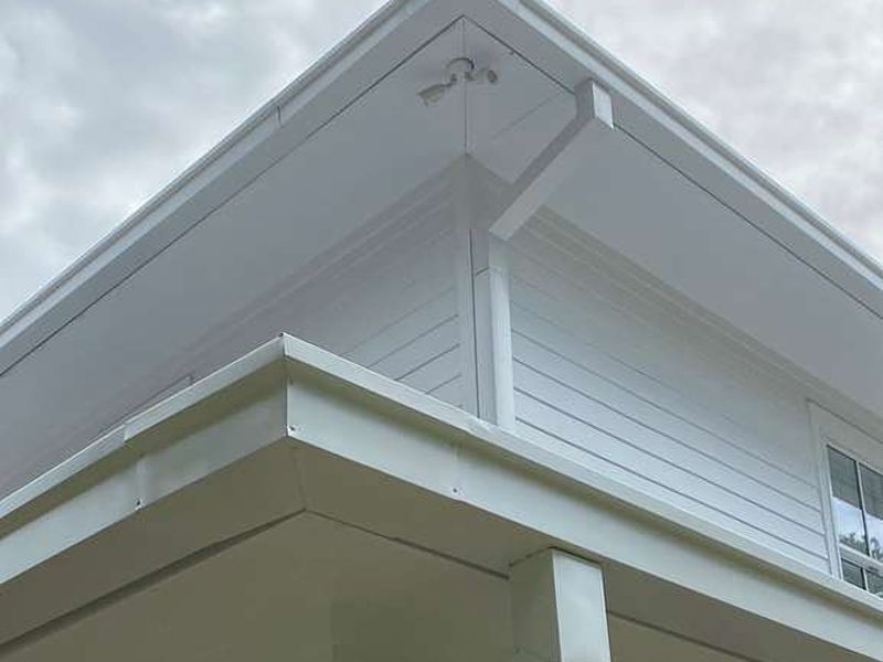 White box gutters and a box downspout on the roof and porch eaves of a white two-story house