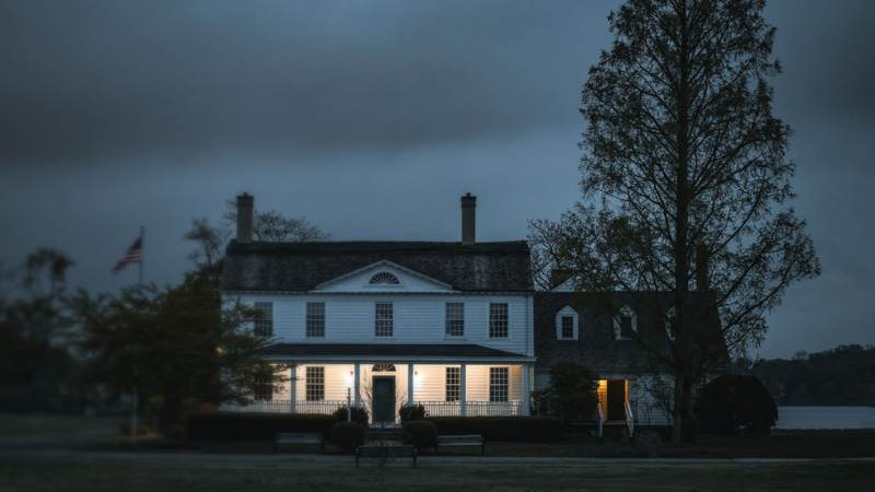 A white colonial-style home with lit windows under a stormy evening sky
