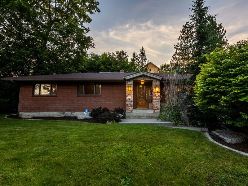 A single-story red-brick ranch house with a stone-trimmed entry and a wide front lawn at dusk