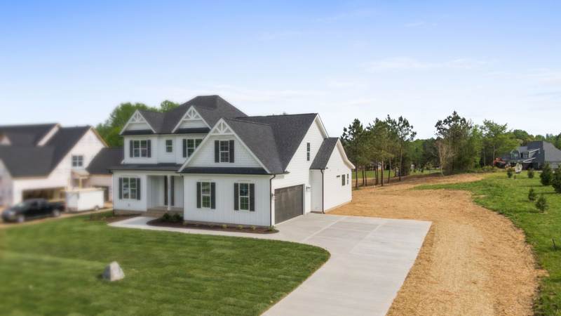 A newly built two-story house with fresh sod and a long concrete driveway on a flat lot at the edge of pine woods