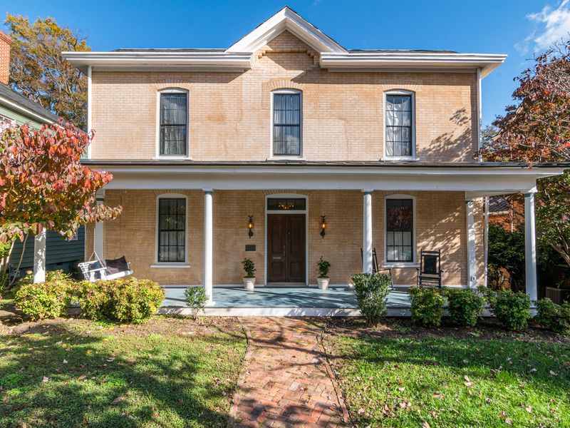 Two-story tan brick house with a full-width front porch, white columns and a brick walk