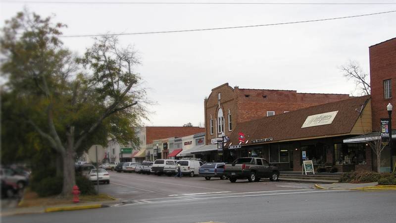 Brick storefronts along a downtown street in Metter, Georgia, with a large oak tree on the corner