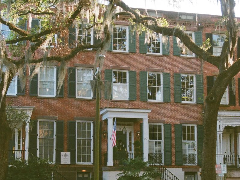 Red-brick Savannah townhouses with green shutters and iron railings under a live oak hung with Spanish moss