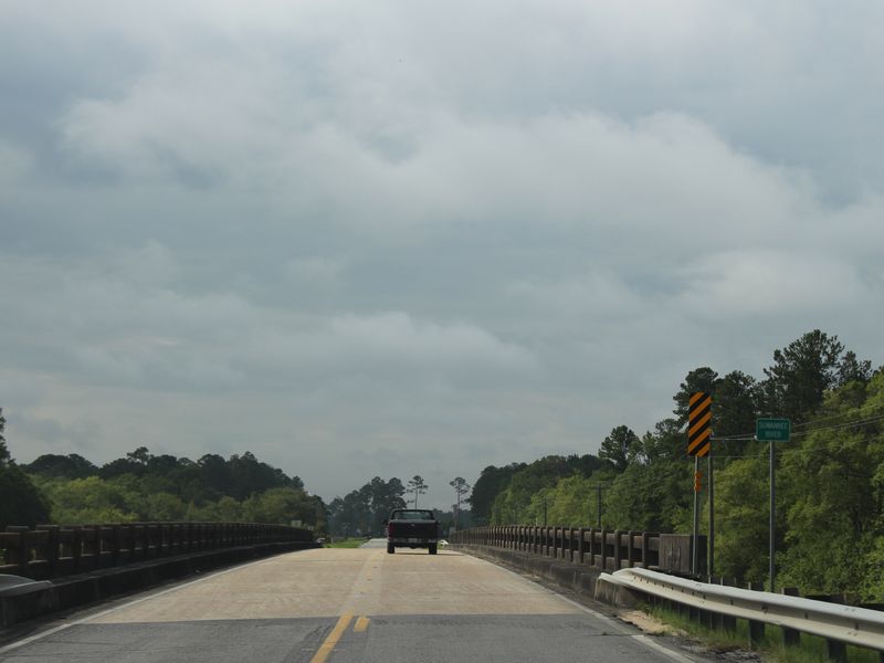 Gray storm clouds over the GA 94 bridge across the Suwannee River at Fargo, Georgia, with a pickup truck crossing between stands of pine and oak