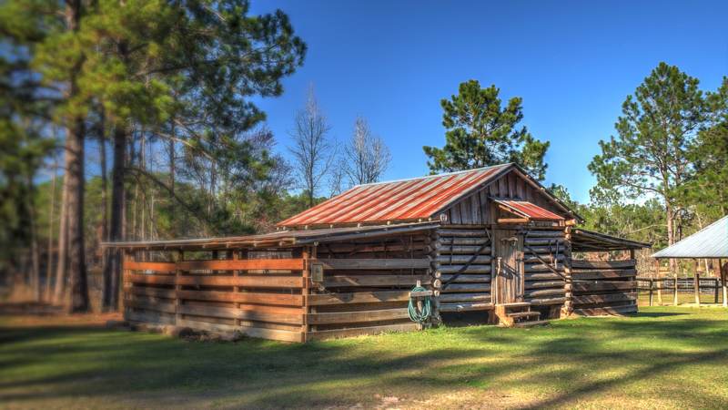 The log mule and hay barn at General Coffee State Park near Douglas, Georgia, with a rust-red metal roof under tall pines