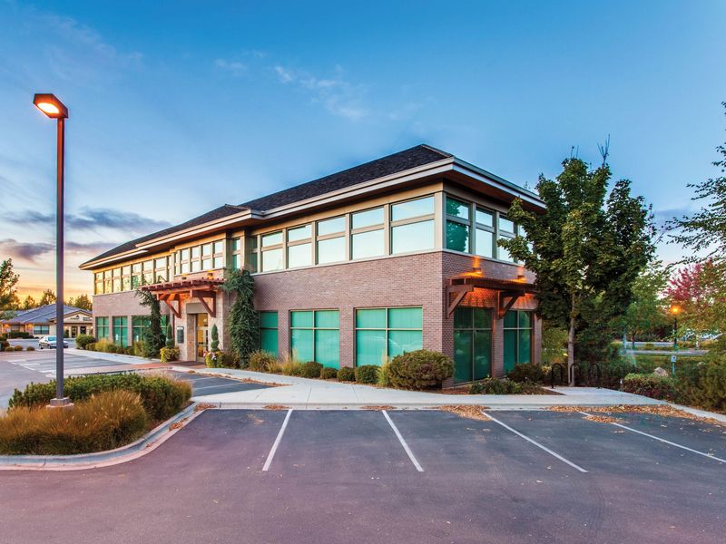 A two-story brick office building with a hipped roof and deep eaves beside an empty parking lot at dusk