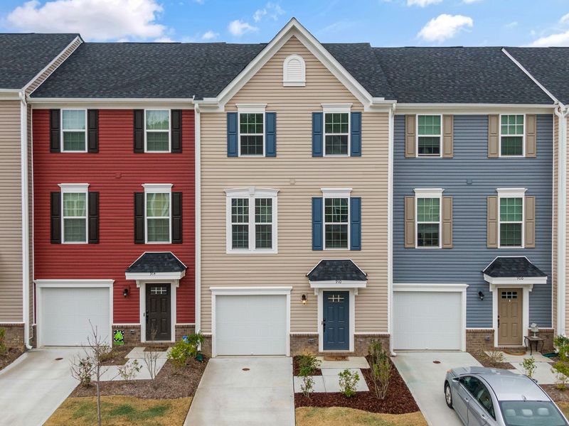 A row of three-story townhouses in different siding colors, each with its own garage and driveway