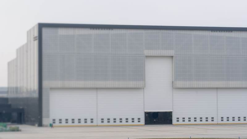 A large modern warehouse with a pale metal facade and a row of closed loading doors