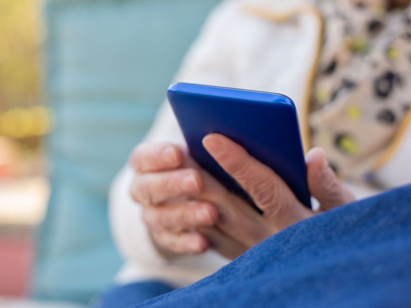 Close-up of an older person's hands holding a blue smartphone outdoors