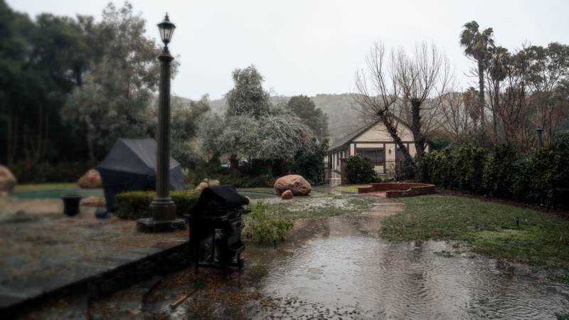 Rainwater running across a stone patio and lawn toward a small cottage during a heavy storm