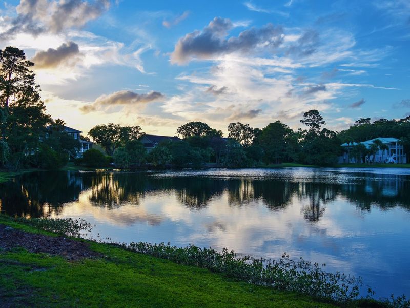 Two-story homes and live oaks reflected in a neighborhood stormwater pond at dusk