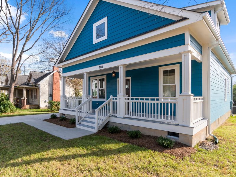 A blue bungalow with a white front porch and a downspout that ends in a short green extension beside the foundation