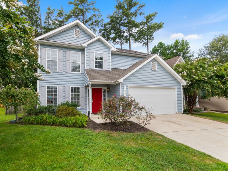 A blue two-story home with a red front door, white gutters and a downspout beside the entry, under tall pines
