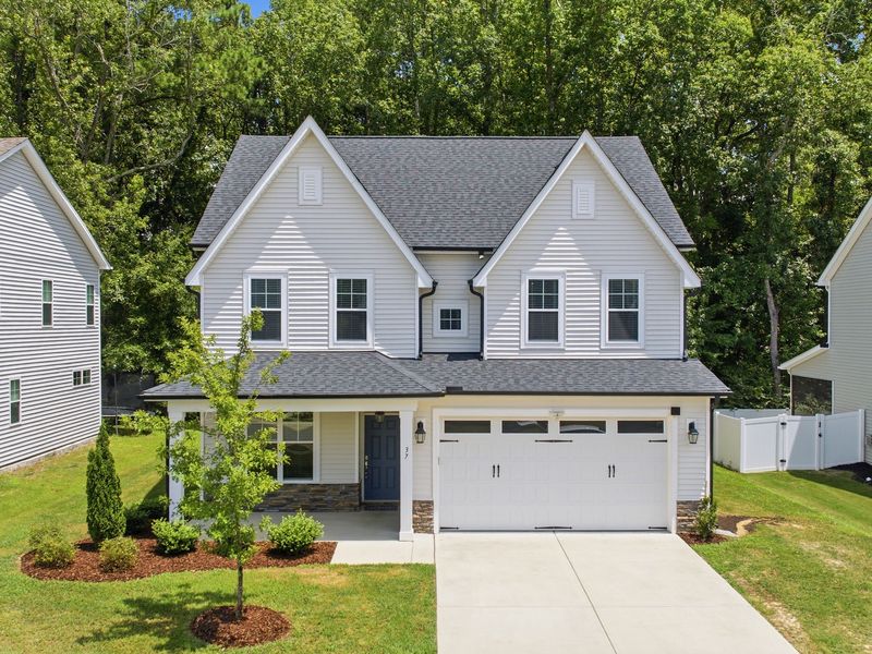 A gray two-story home with twin front gables, a covered porch and white gutters, backed by woods