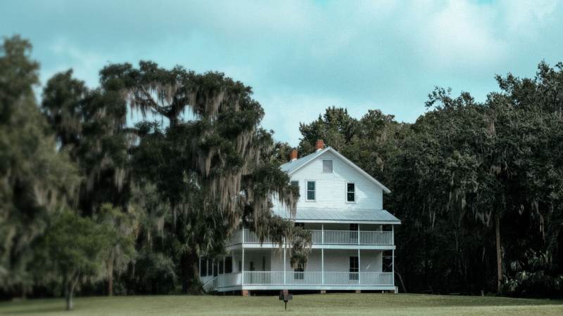 A white two-story farmhouse with wraparound porches beneath live oaks hung with Spanish moss