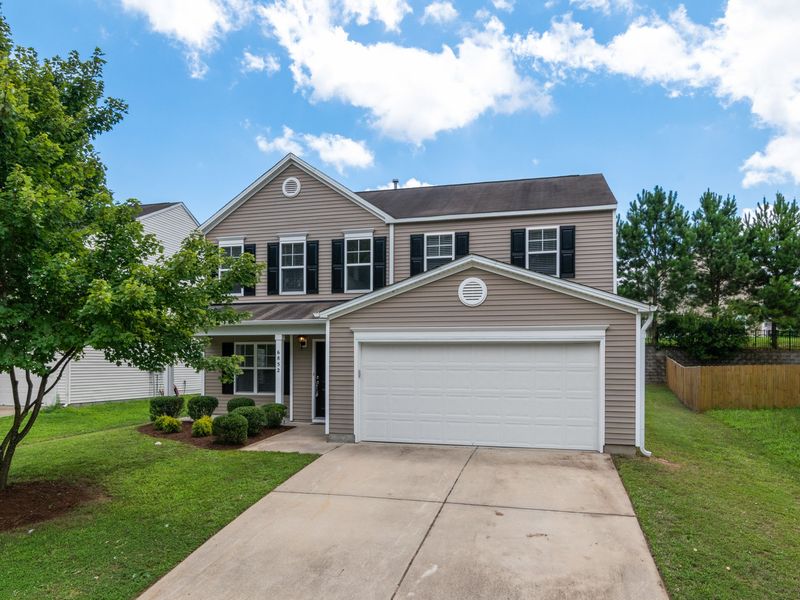 A two-story suburban house with a front-facing garage, white trim and a young tree in the front yard