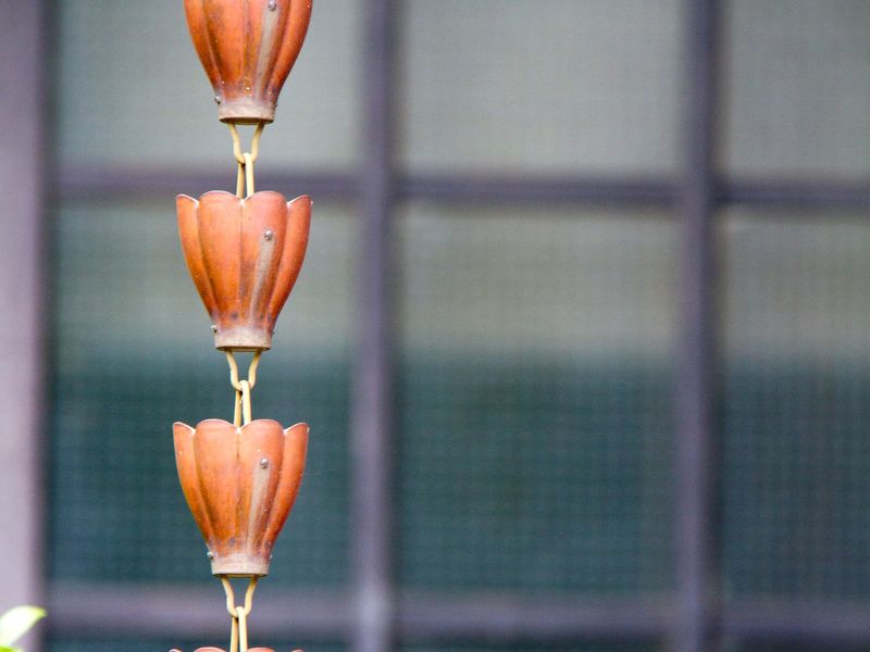 Copper cup-style rain chain hanging in front of a porch window