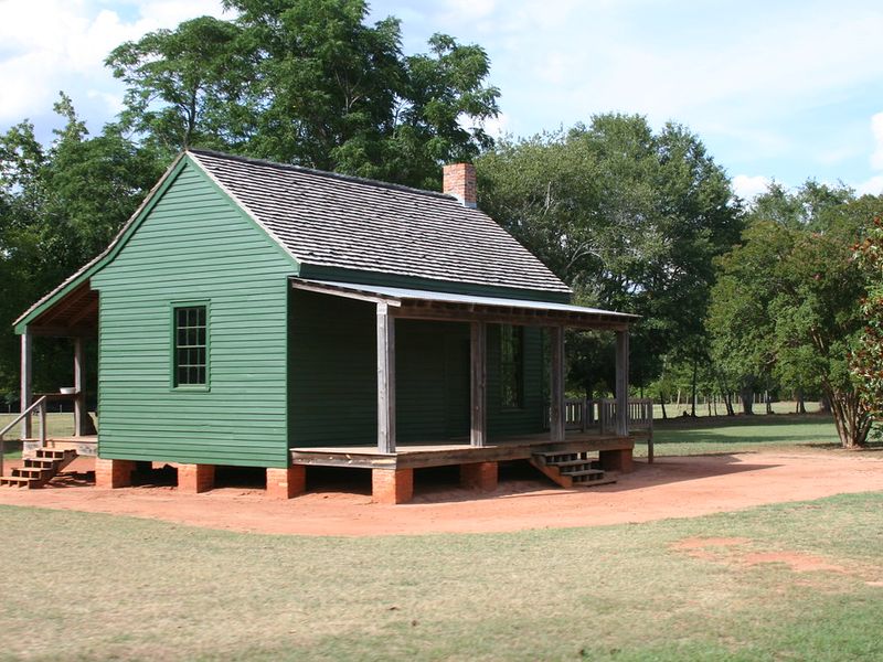Green wood-sided Georgia farmhouse with a tin-roofed porch, raised on brick piers over red clay