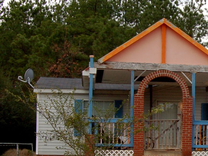 Manufactured home with vinyl siding, blue shutters and a brick-arched front porch under tall pines