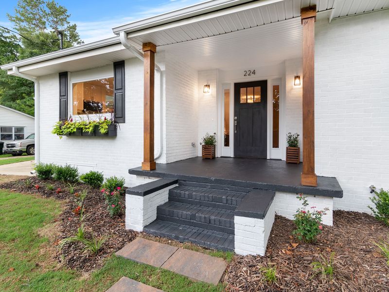 A white-painted brick house with black shutters, a covered front porch and white gutters