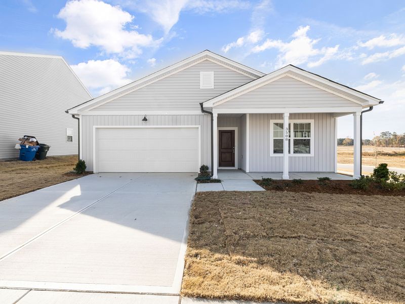 A new single-story house with light gray siding, dark downspouts, a covered front porch and a two-car garage on a flat, freshly sodded lot