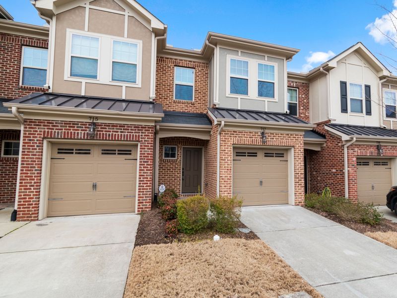A row of brick-front townhouses with single garages, metal porch roofs and white downspouts at each unit