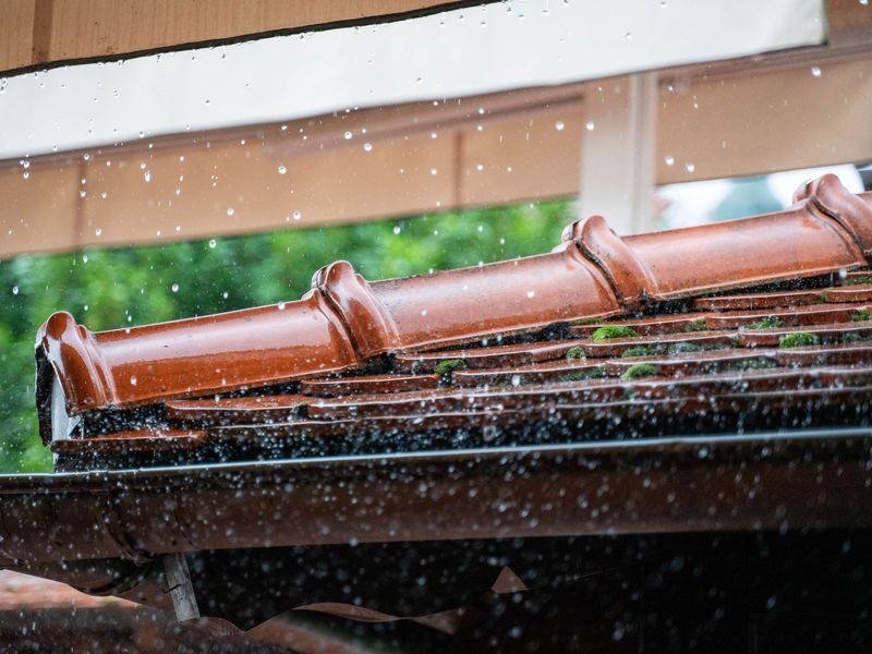 Rain running off a row of red clay roof tiles into the gutter below