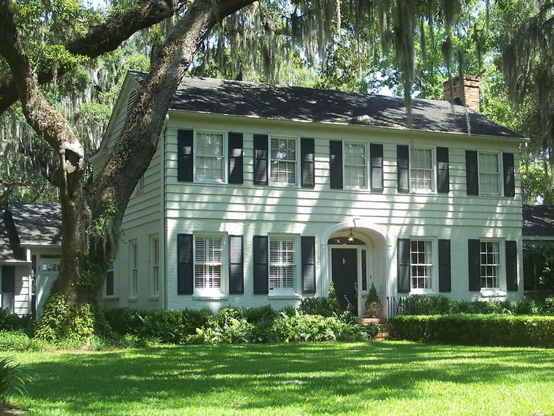 White two-story colonial house with dark shutters under live oak limbs hung with Spanish moss in the Ortega neighborhood of Jacksonville