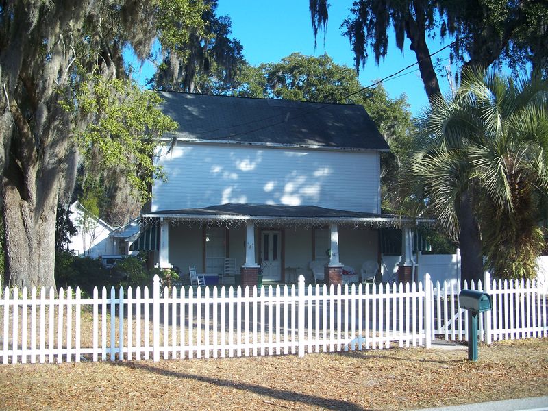 White two-story frame house with a front porch behind a white picket fence under moss-draped oaks in Orange Park