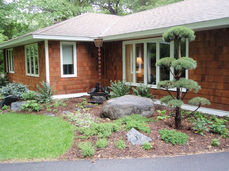 A cup-style rain chain running from a leader head into a stone basin in a planted front-yard bed
