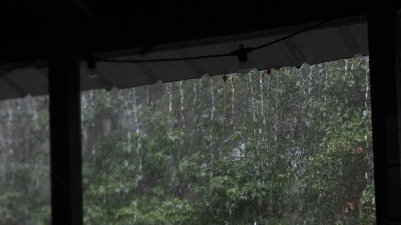Heavy rain pouring off a porch roof edge in front of a wooded backyard