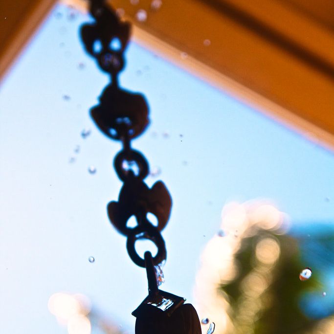 Water droplets spilling from the cups of a dark metal rain chain against the sky