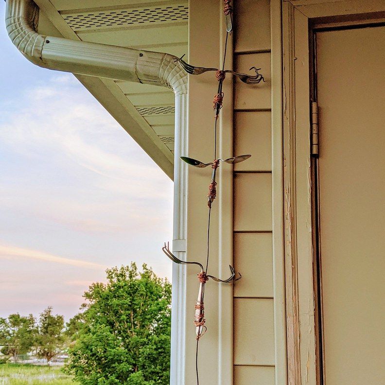 A homemade rain chain hanging beside a front door, next to a white downspout