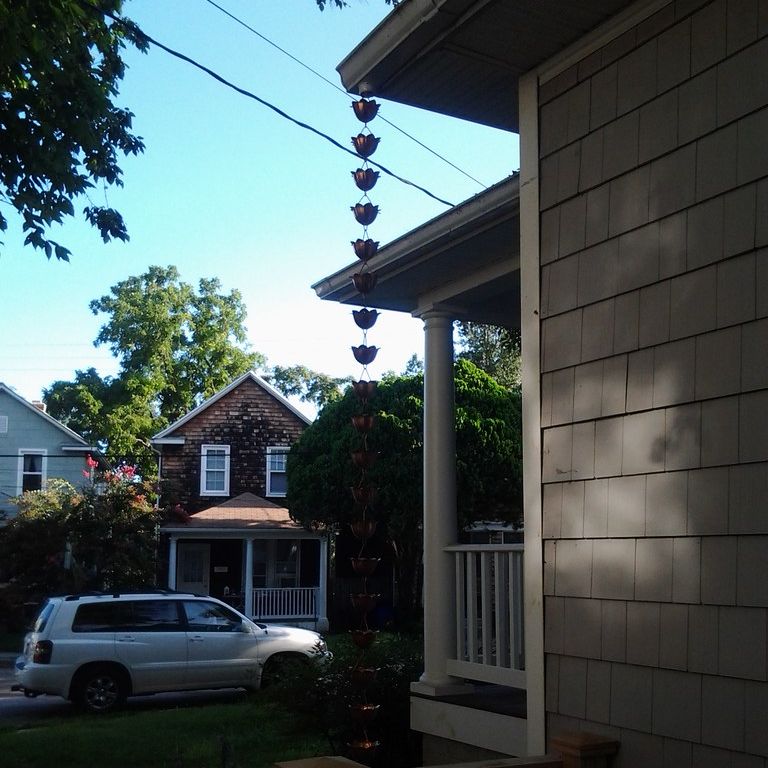 A cup rain chain hanging from the corner of a front porch roof on a residential street