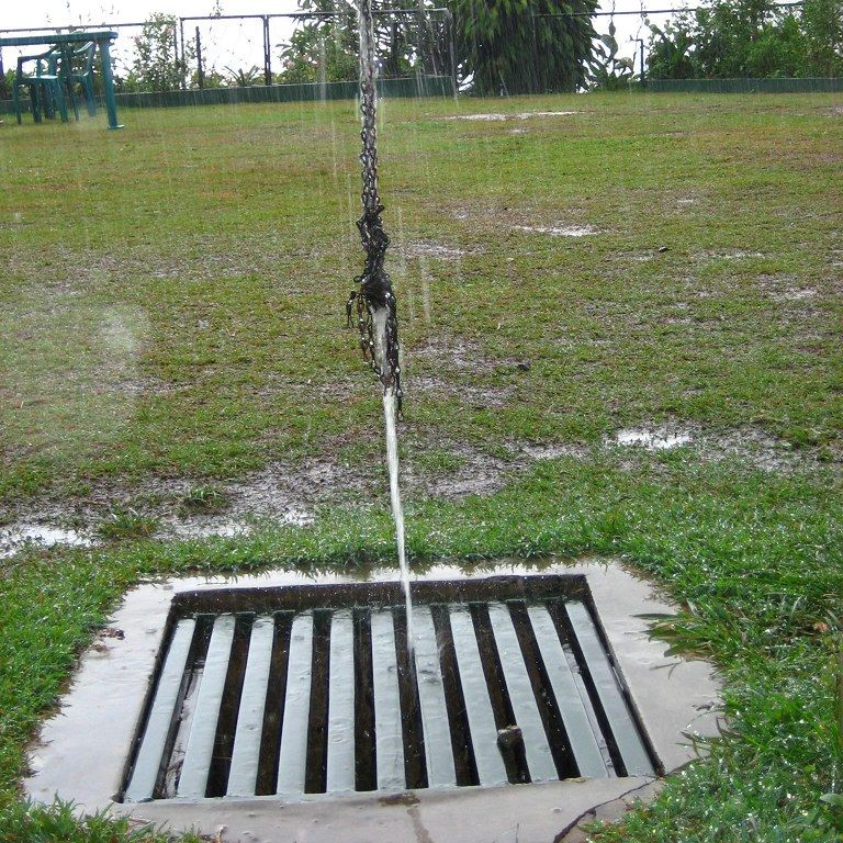 A rain chain carrying water down into a grated drain set in a lawn