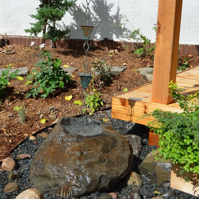 A verdigris rain chain above a boulder basin and a bed of dark gravel
