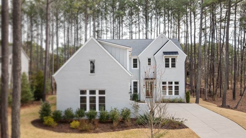 A white two-story house standing among tall pines, with pine straw on the ground around it