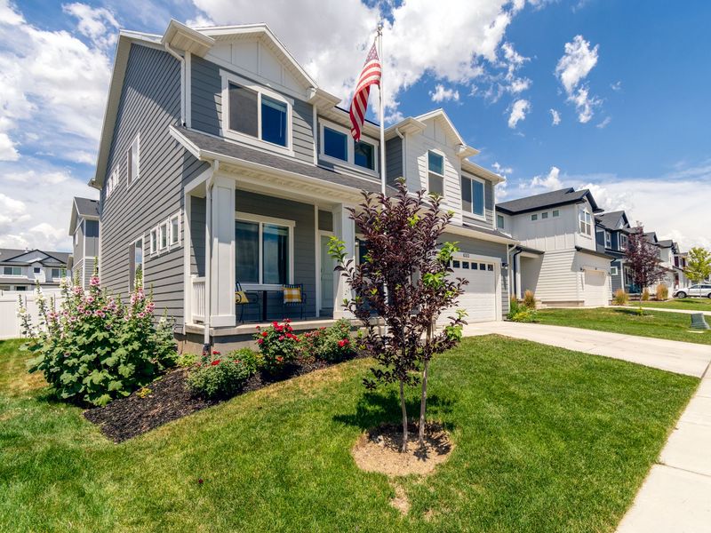 A gray two-story home with a front porch and an American flag on a neighborhood street