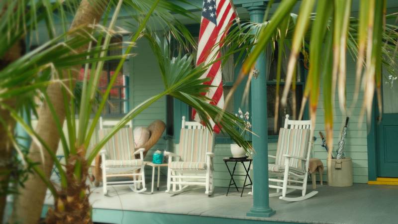 Rocking chairs and an American flag on a Southern front porch framed by palm fronds