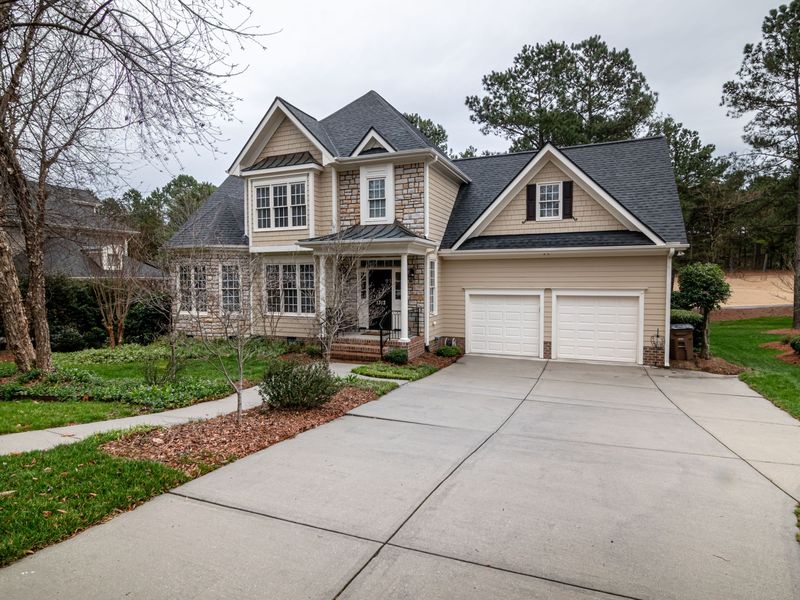 A two-story house with a double garage and a wide concrete driveway, framed by pines