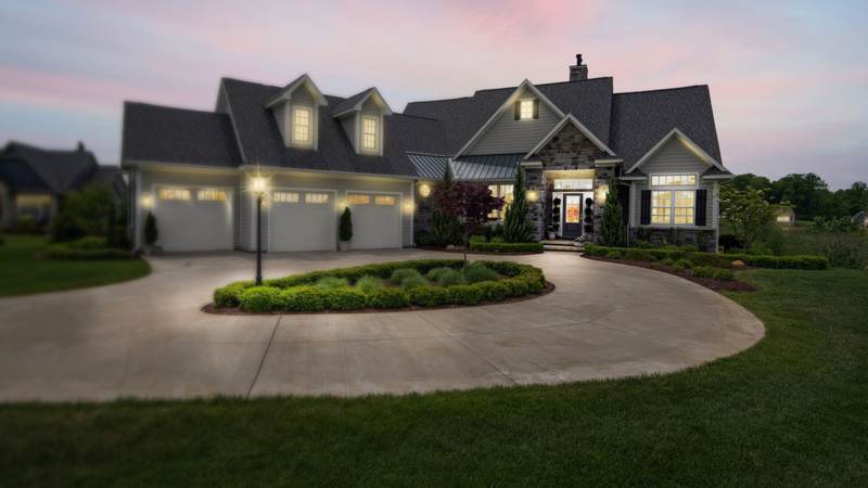 A large two-story home at dusk with long eaves, several gables and a circular driveway