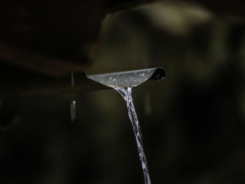 Rainwater pouring in a steady stream from the open end of a metal gutter